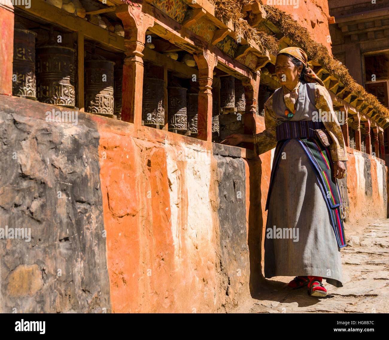 Native woman walking along Mani Wall and spinning prayer wheels, Kagbeni, Mustang District, Nepal Stock Photo