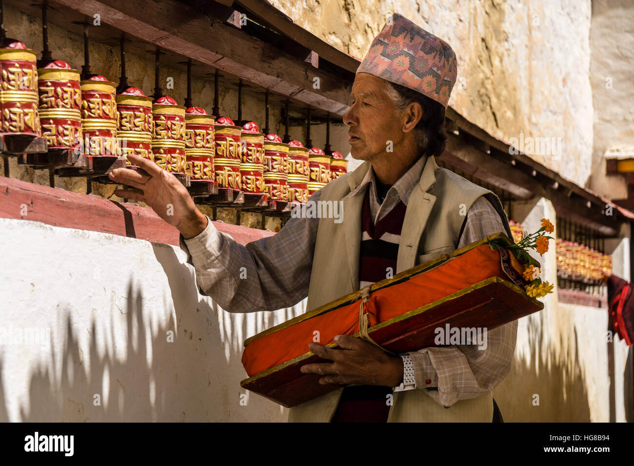 Local man, carrying a prayer book, is walking along the wall with spinning prayer wheels, Marpha, Mustang District, Nepal Stock Photo