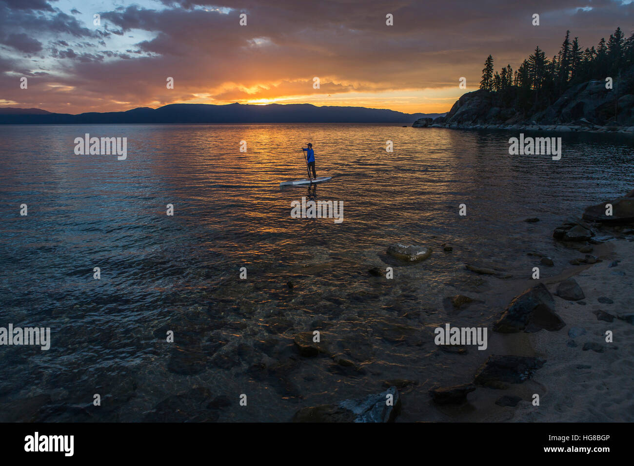 Man paddleboarding in lake during sunset Stock Photo