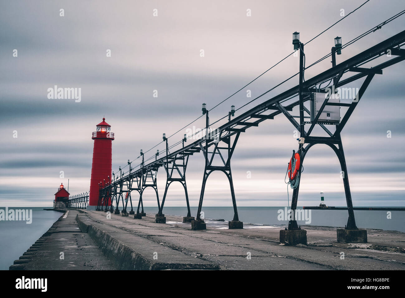 Electricity pylon and lighthouse on pier amidst sea against cloudy sky Stock Photo