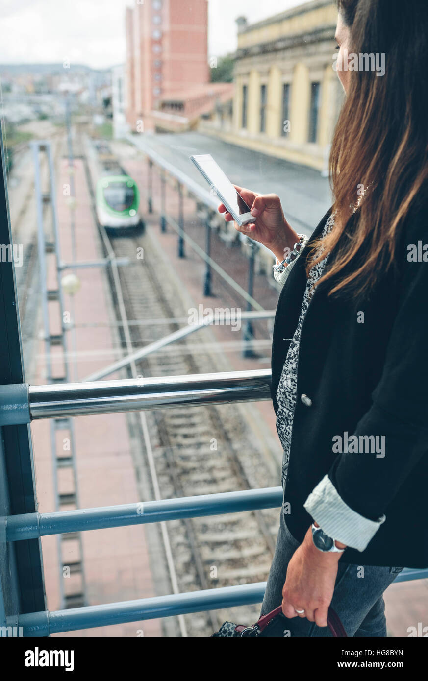 Side view of woman using phone while standing on footbridge over railroad track Stock Photo