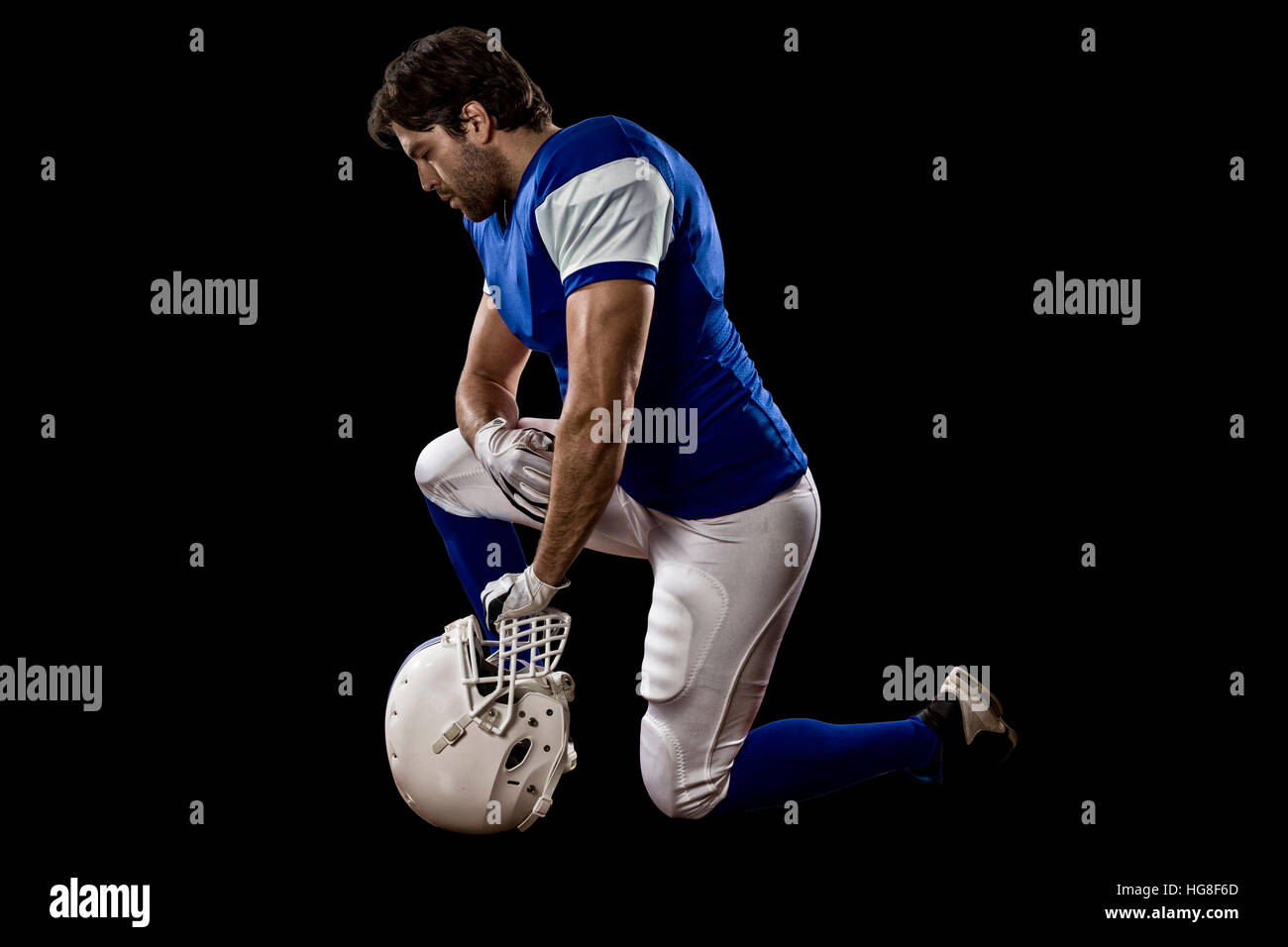 Football Player with a blue uniform on his knees, on a black background
