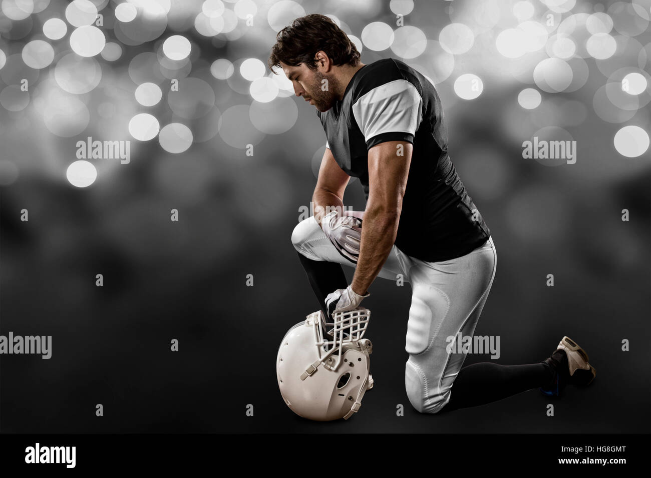 Football Player with a black uniform on his knees, on a black lights