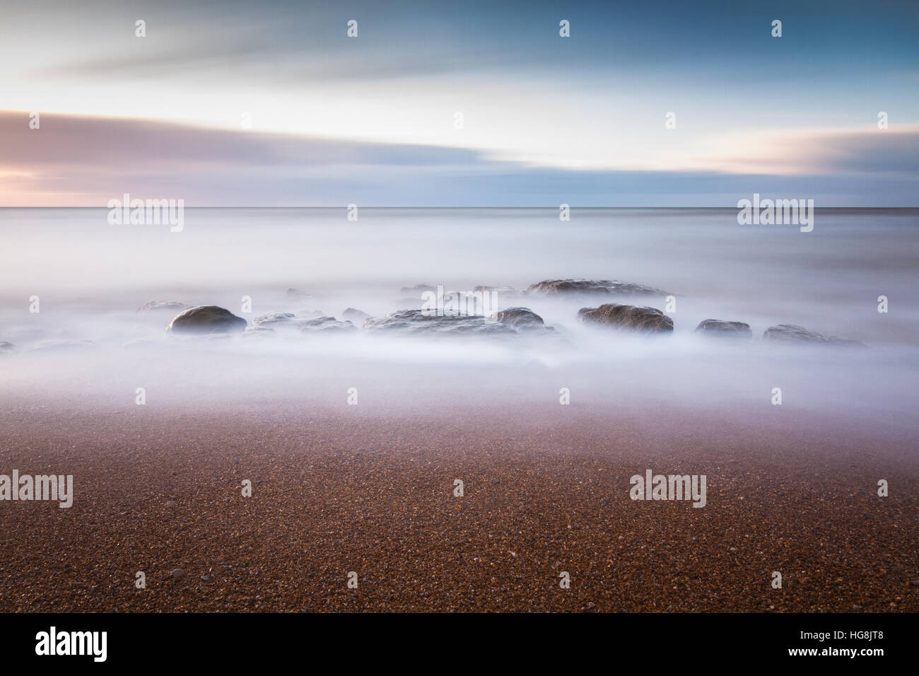 Rocks on the beach being submerged by the incoming tide during sunset Stock Photo