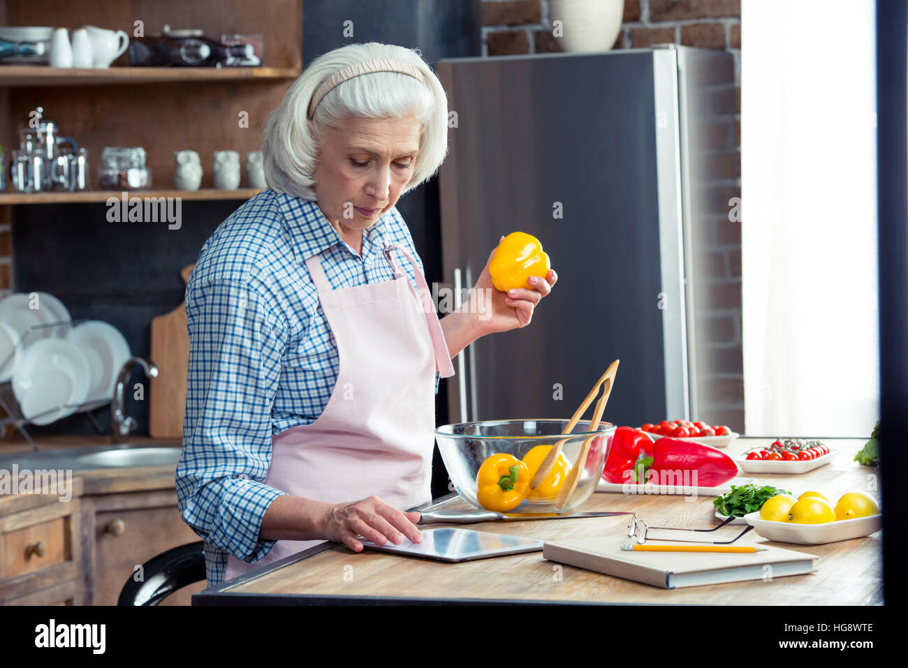 Senior woman using digital tablet in kitchen while preparing vegetable salad Stock Photo