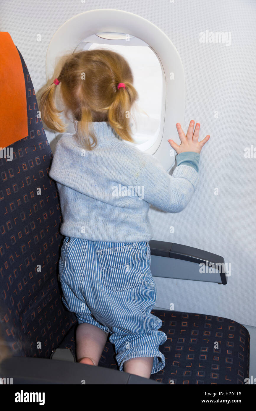 Kid child / toddler / children age 2 on holiday vacation looking looks look out from window seat while flying on air plane / airplane aeroplane flight Stock Photo