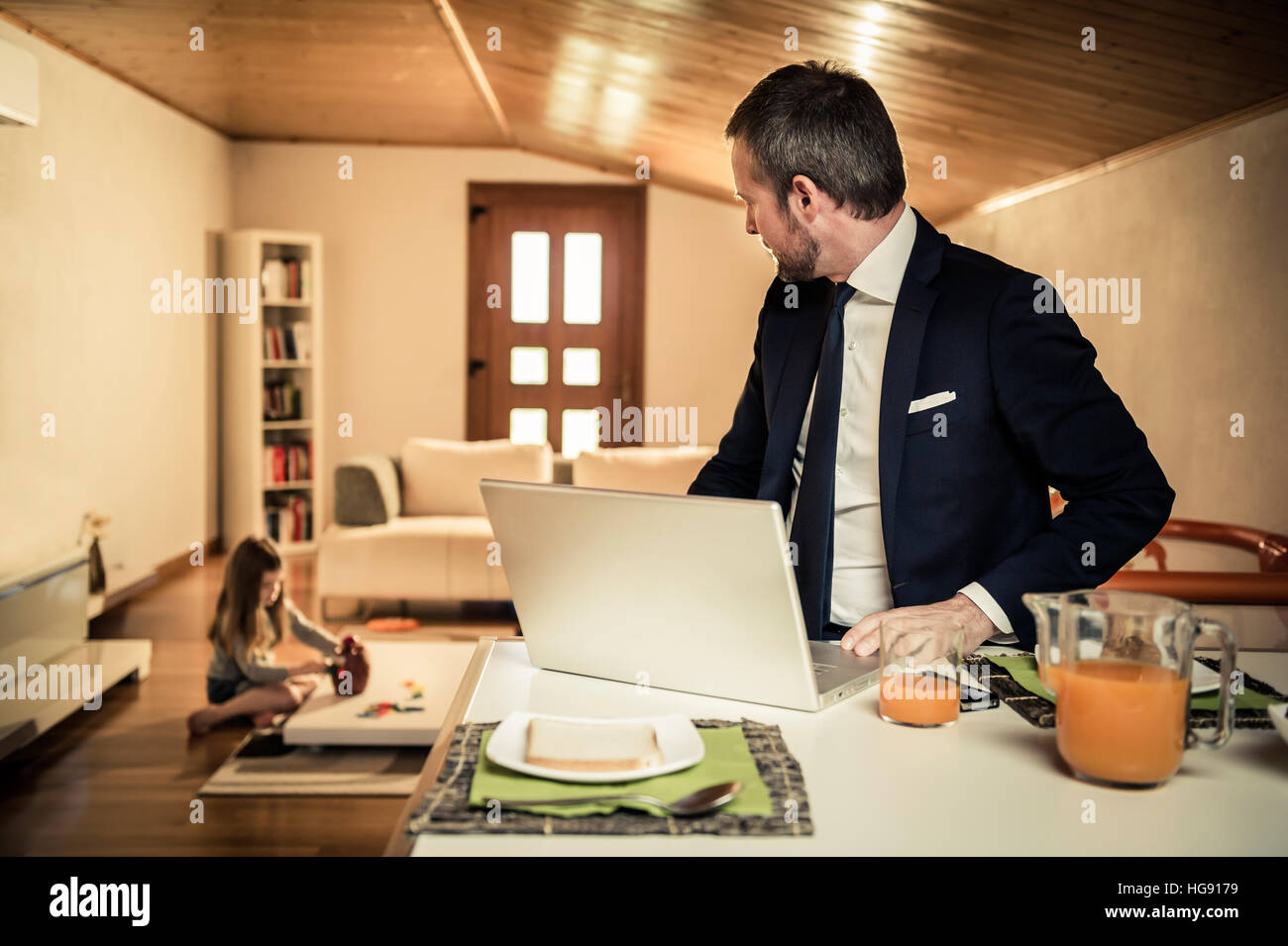 Young father working at home during breakfast while his little girl is playing on the floor Stock Photo