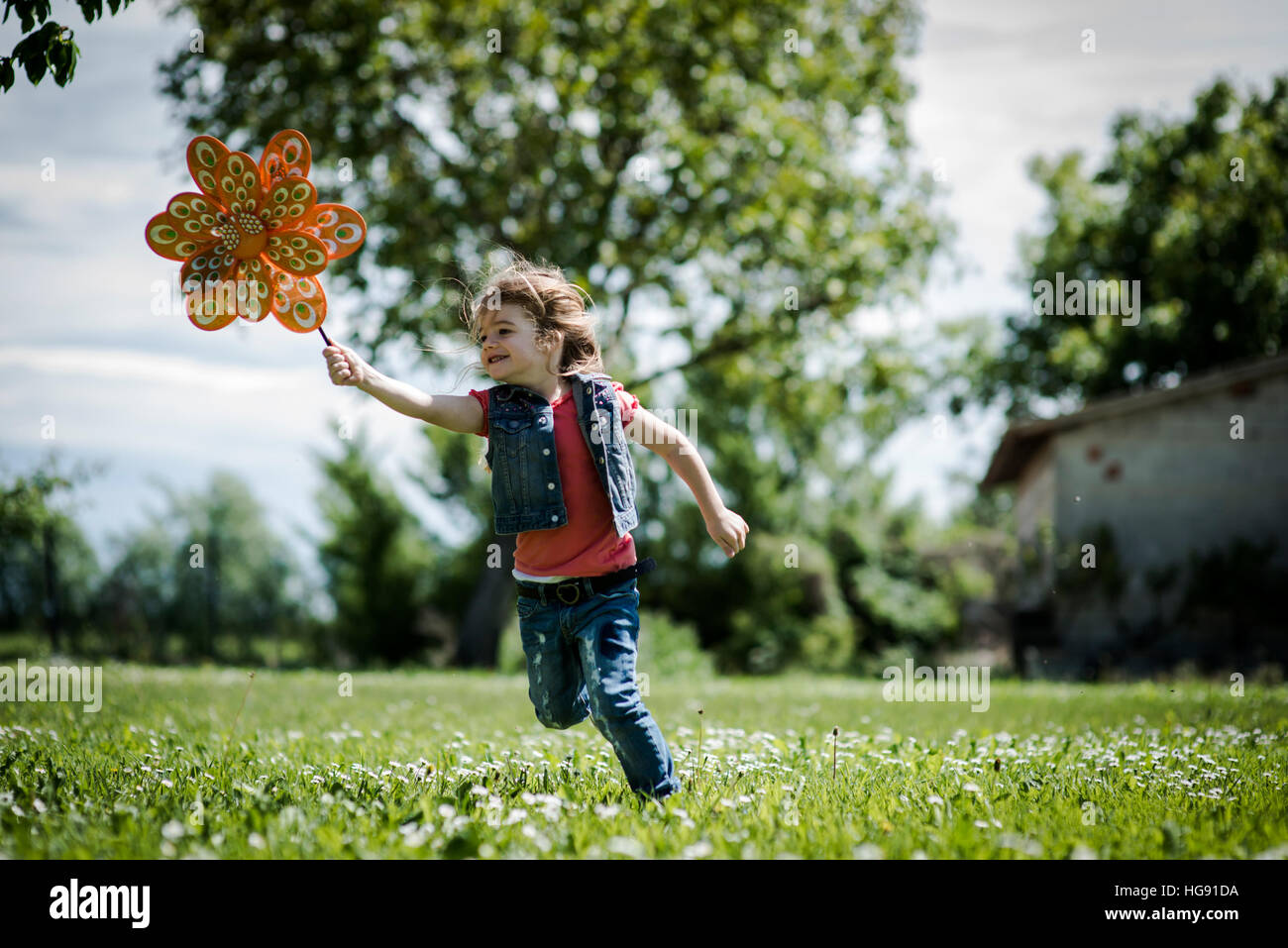 Little girl playing outdoors, running with pinwheel Stock Photo
