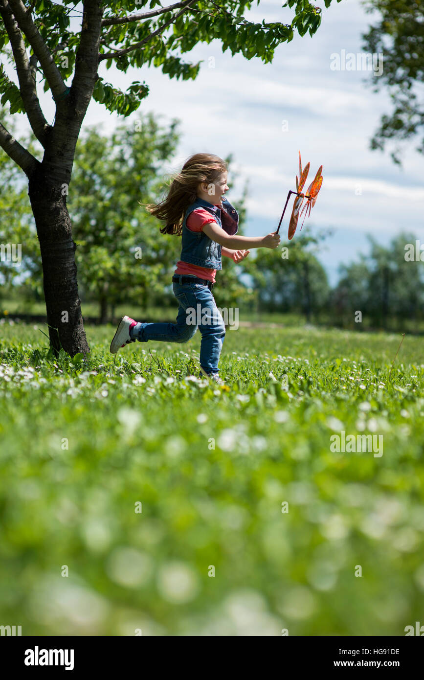 Little girl playing outdoors, running with pinwheel Stock Photo