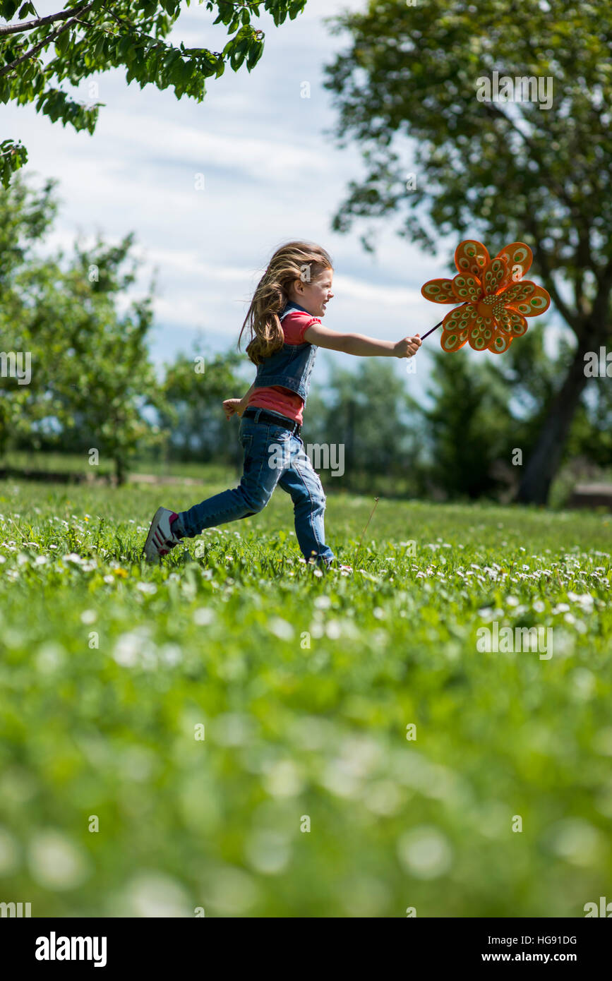 Little girl playing outdoors, running with pinwheel Stock Photo