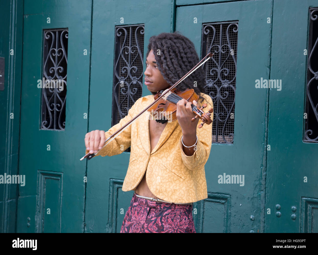 A busker plays the violin in New Orleans French Quarter.  Typical wrought iron decoration on the wooden door in the background. Stock Photo