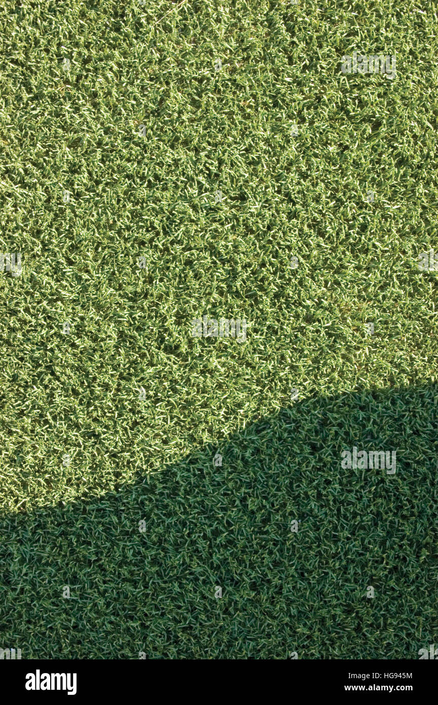 Artificial grass fake turf synthetic lawn field macro closeup with gentle shaded shadow area, green sports texture background shade Stock Photo