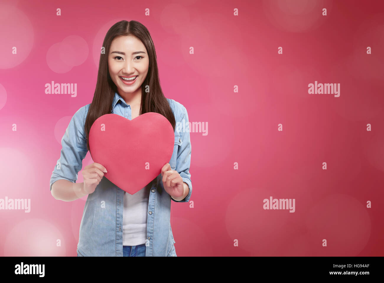 Beautiful asian woman holding red heart shape smiling over pink ...