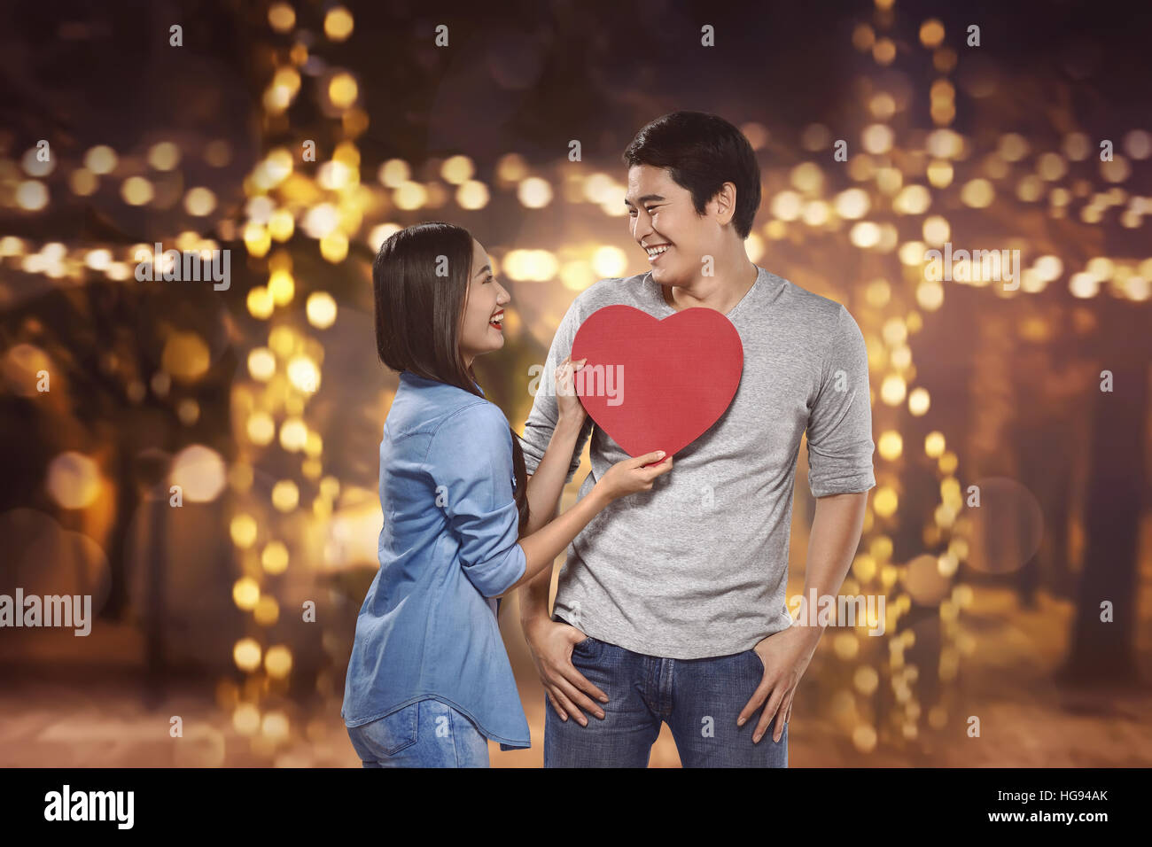 Smiling asian couple holding red heart shape against blurred light ...