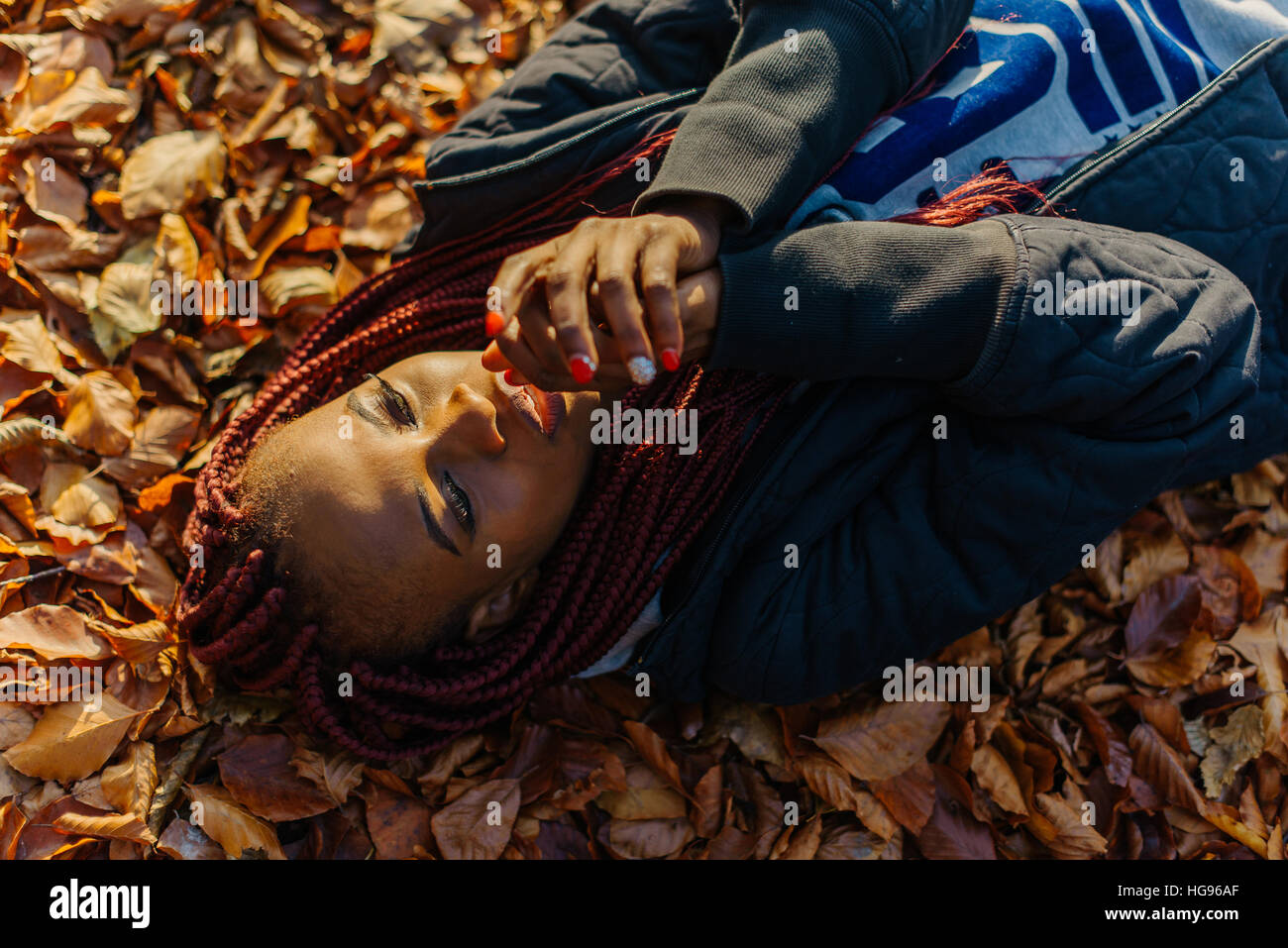 Beautiful african american girl lying in yellow leaves in autumn park. Female making selfi and smiling Stock Photo