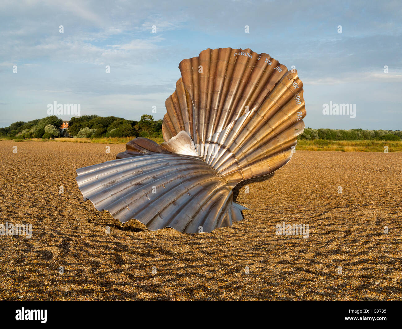 'The Scallop' sculpture by Maggi Hambling on the shingle beach at Aldeburgh Suffolk England against a blue sky and trees Stock Photo