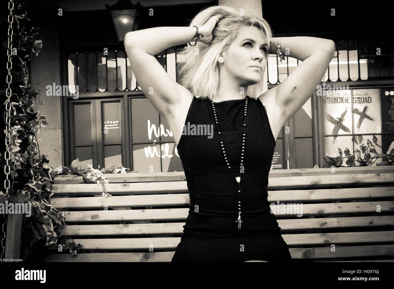 Blonde model poses on bench wearing black dress and Gothic cross Stock Photo