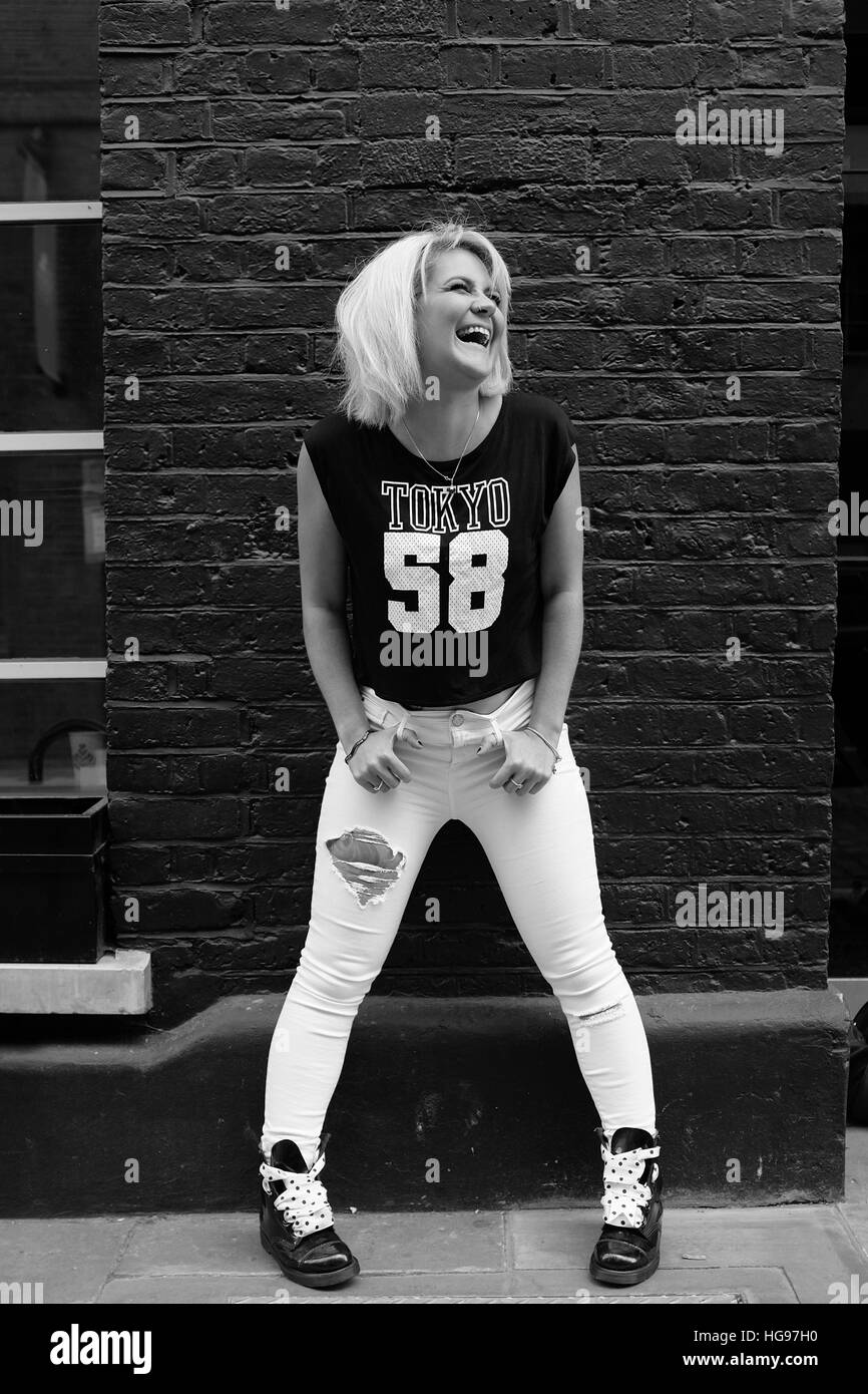 Blonde, punk rock model laughs as she poses in front of brick wall Stock Photo