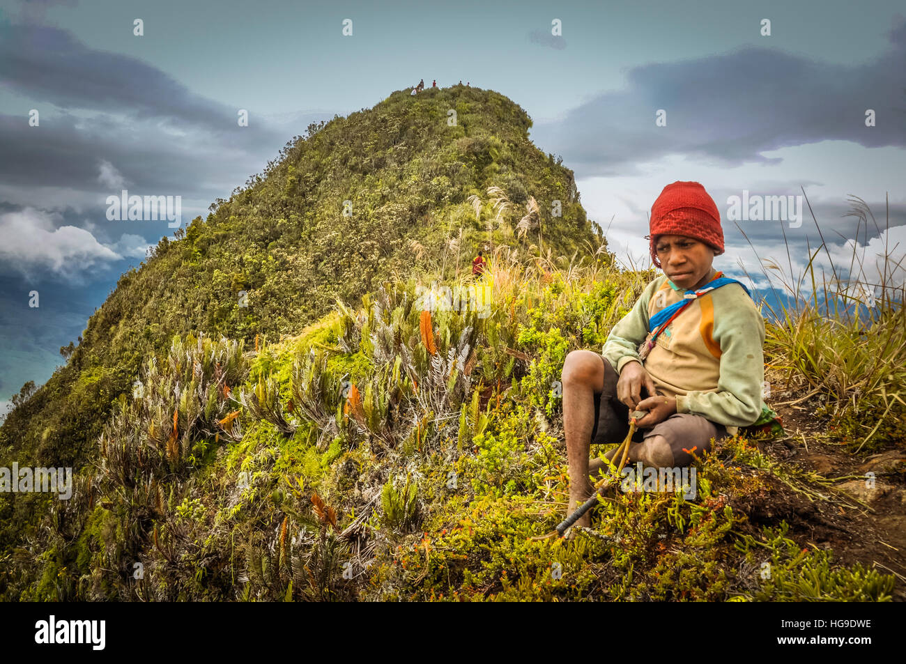 Sara village, Mt. Michael, Papua New Guinea - July 2015: Young native boy with red cap sits on ground near top of mountain and looks sadly down in Sar Stock Photo
