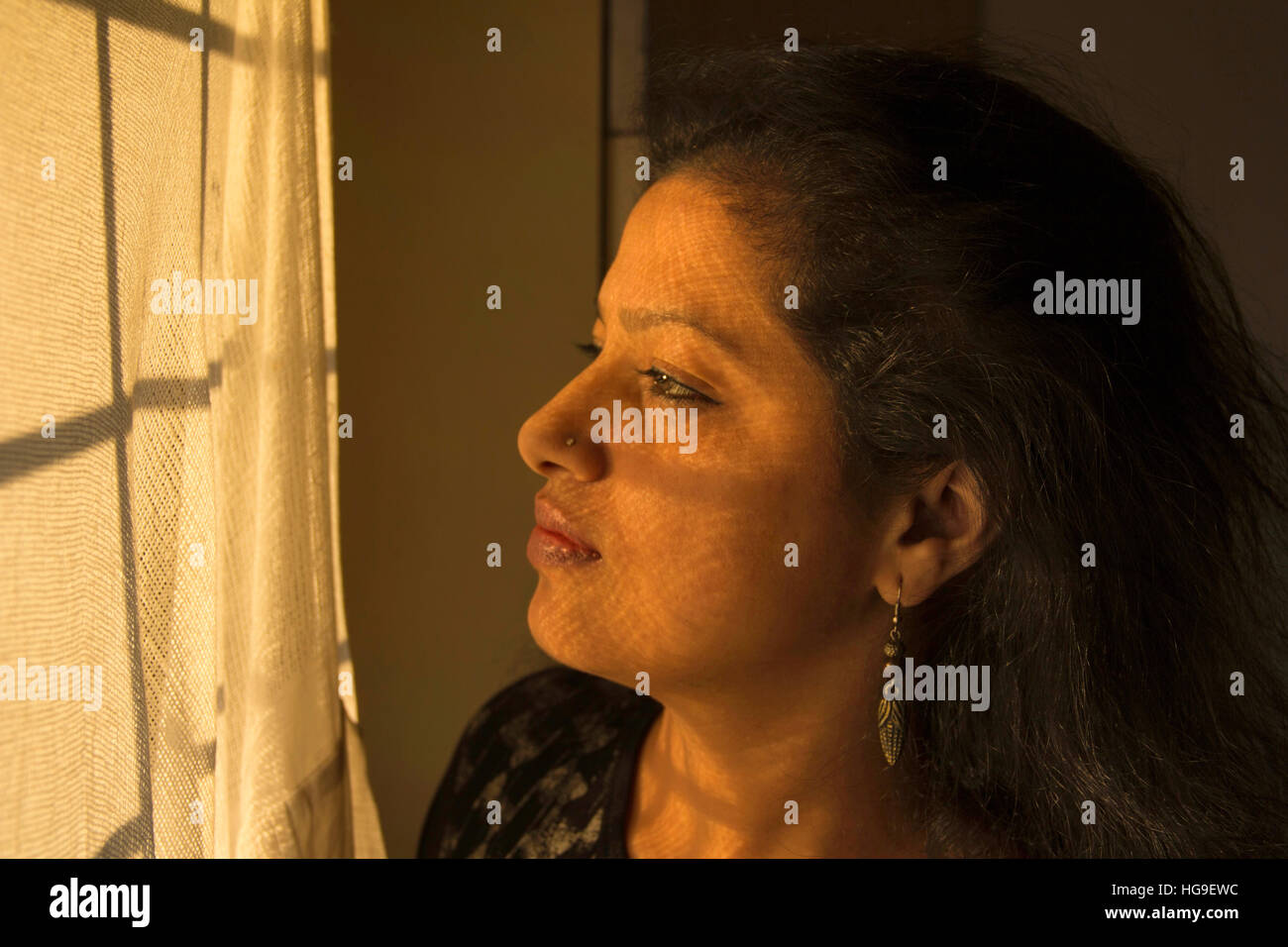 Young Indian woman looking at window with golden light on her face Stock Photo
