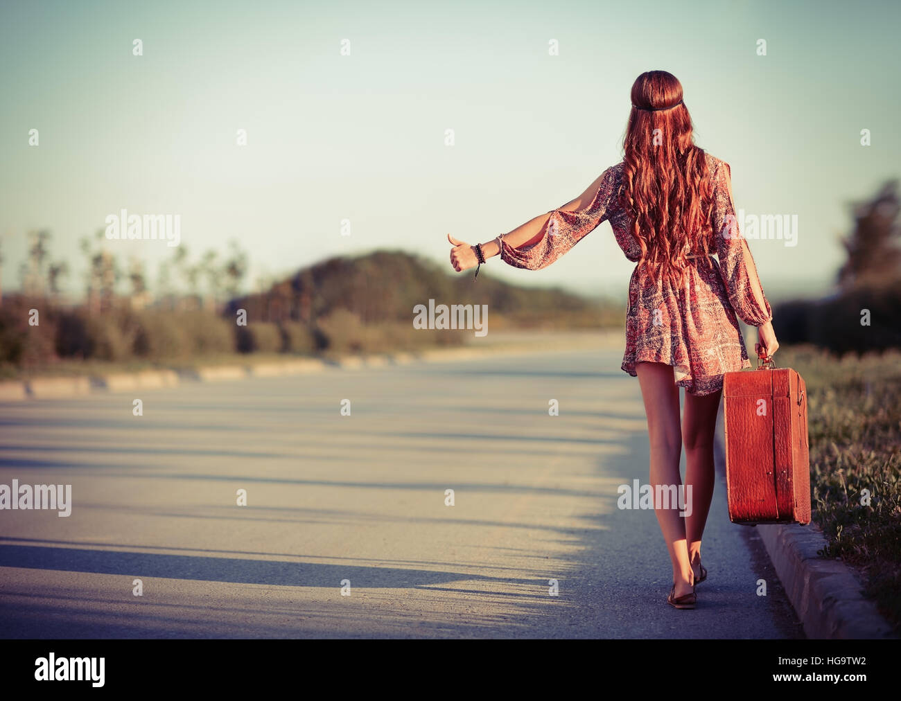 Young hippie woman hitchhiking on the road. Rear view Stock Photo