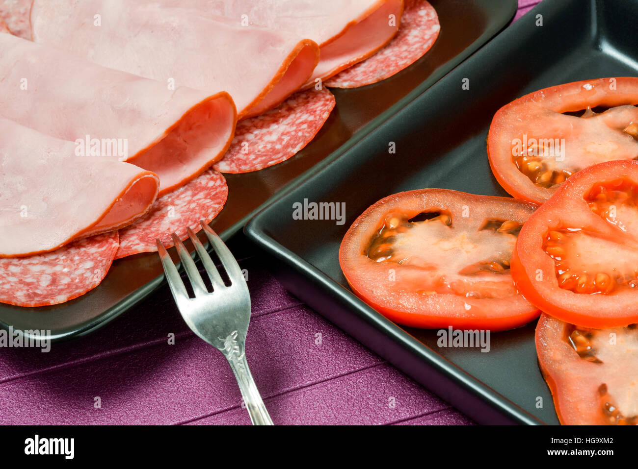 Plates with tomatoes, ham, sausages on the table Stock Photo