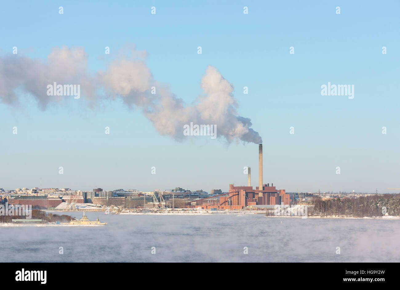Factory with a tall smoking chimney behind vaporing water at winter Stock Photo