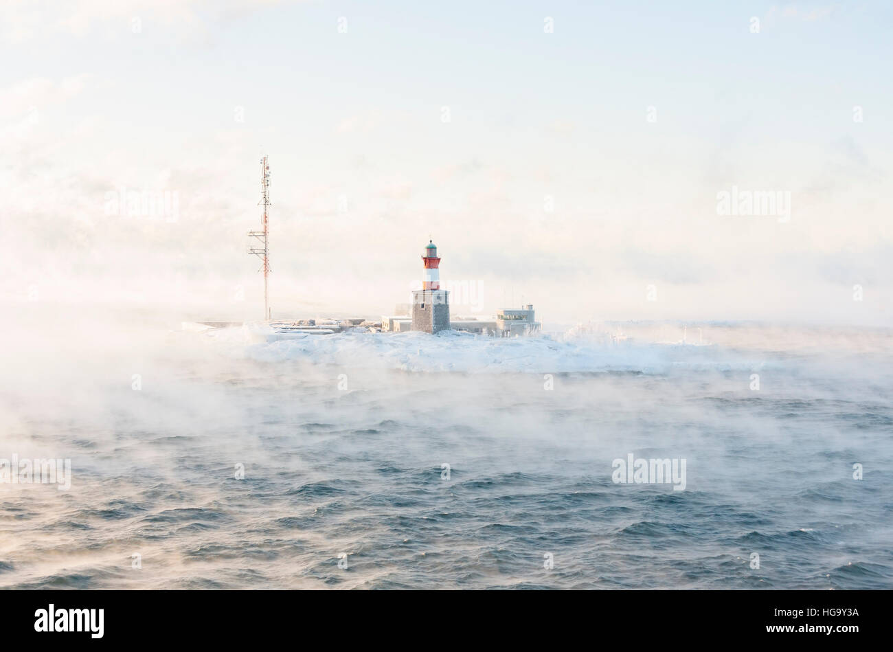 Lighthouse and telecommunication antenna on an isle in a vaporing sea at winter Stock Photo