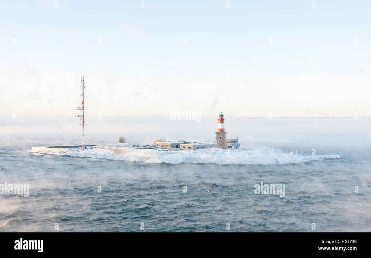 Lighthouse and telecommunication antenna on an isle in a vaporing sea at winter Stock Photo