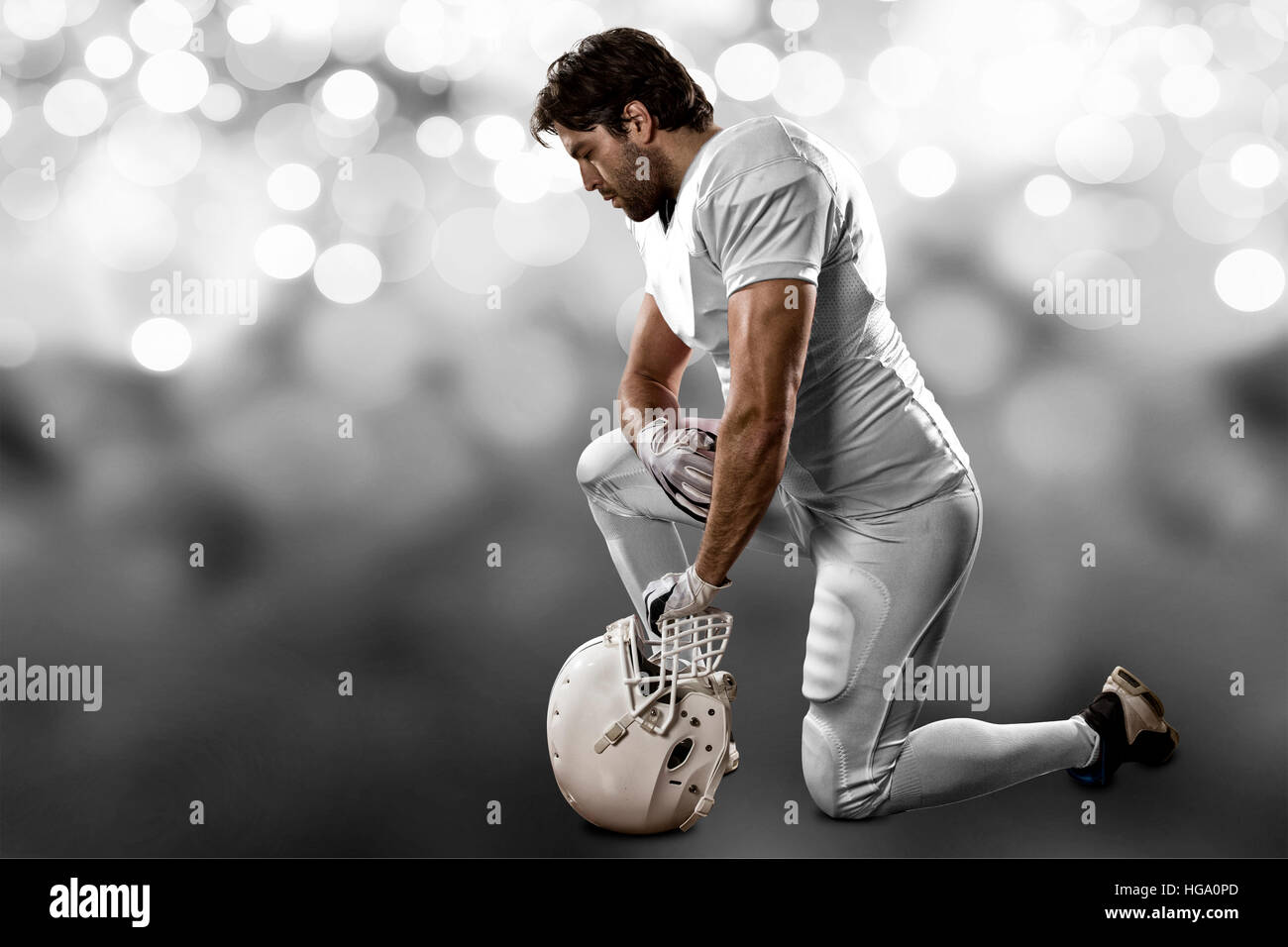 Football Player with a white uniform on his knees, on a white lights
