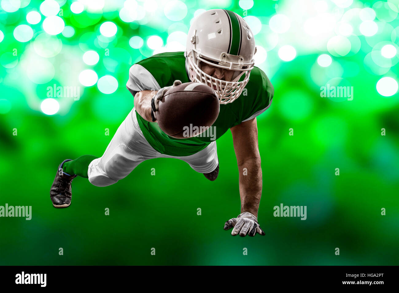 Football Player with a green uniform scoring on a green lights background. Stock Photo