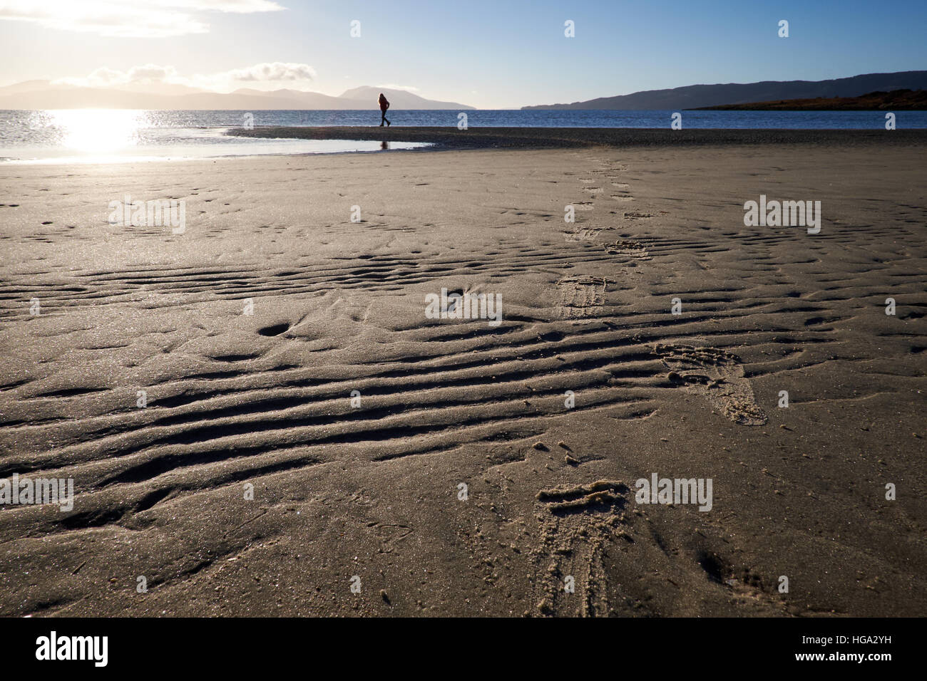 Kilbride bay sands at low tide showing the sand banks, surrounding hills and a clear sky. A figure stands in the distance. Stock Photo