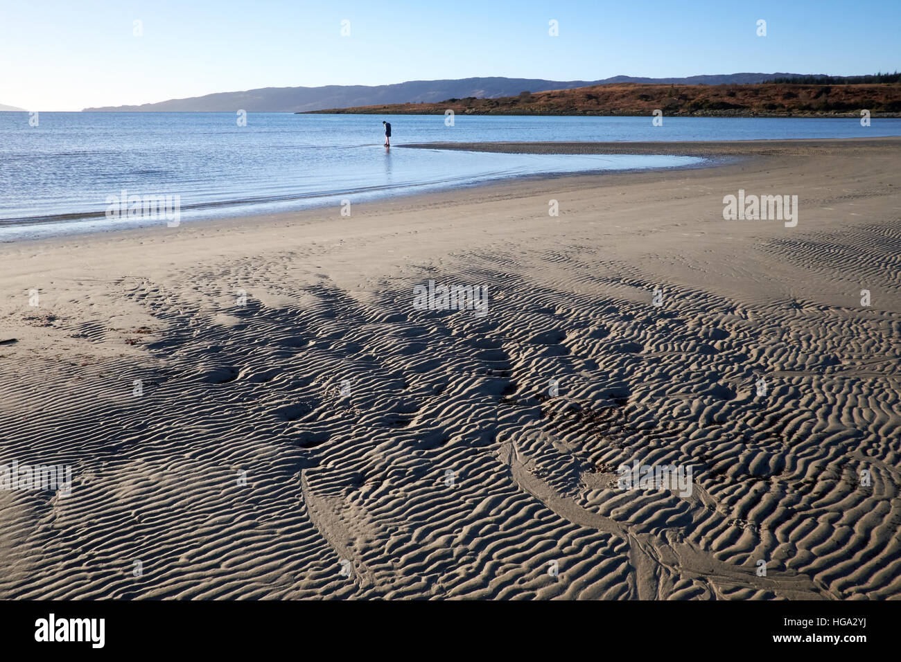 Kilbride bay sands at low tide showing the sand banks, surrounding hills and a clear sky. A figure stands in the distance. Stock Photo