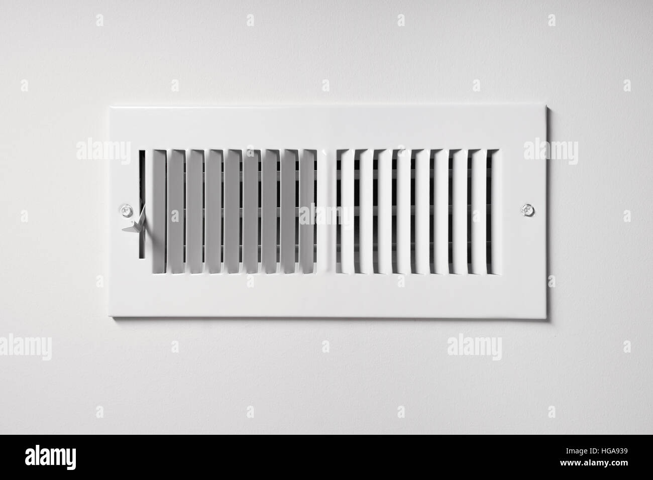 A heating/cooling vent register on the wall of a home, with open/close lever Stock Photo