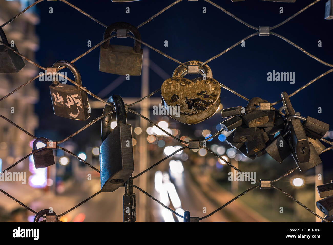 Locks on a metal wire fence with car light trails in the background Stock Photo