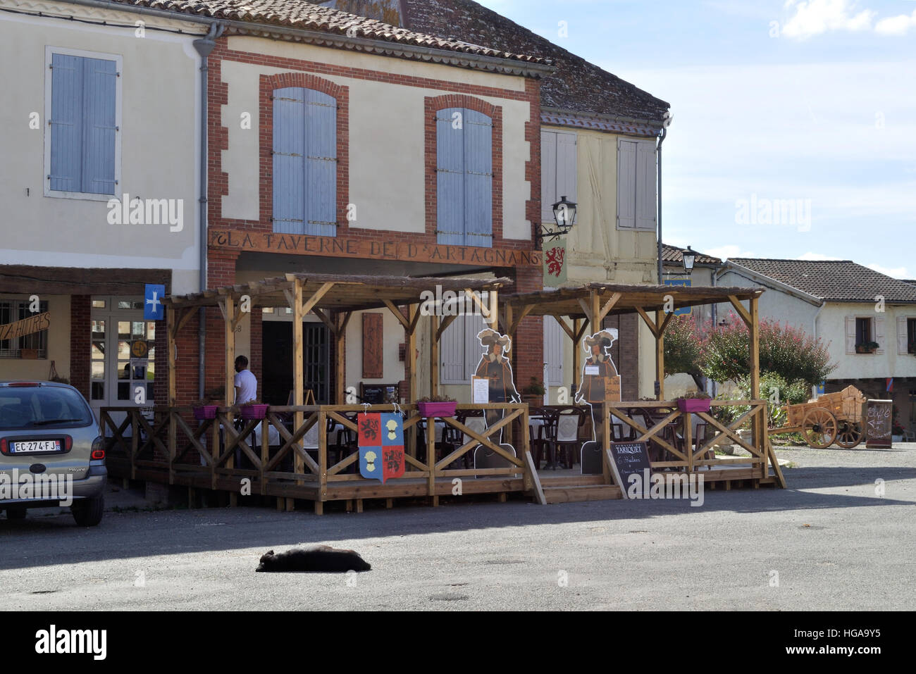 La Taverne d'Artagnan, a restaurant and cafe in Place d'Artagnan, Lupiac, France. A local dog soaks up the sunshine! Stock Photo