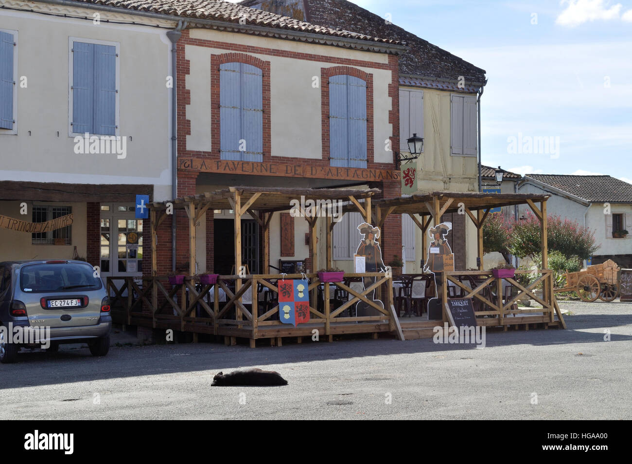 La Taverne d'Artagnan, a restaurant and cafe in Place d'Artagnan, Lupiac, France. A local dog soaks up the sunshine! Stock Photo