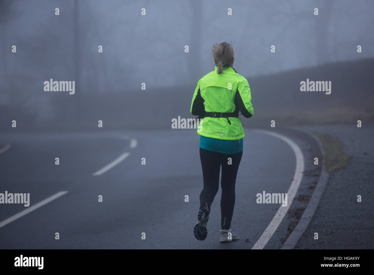 A female jogger wearing Hi Viz while jogging along the B4343 as the thick fog hampers visibility this morning. © Ian Jones/Alamy Live News Stock Photo