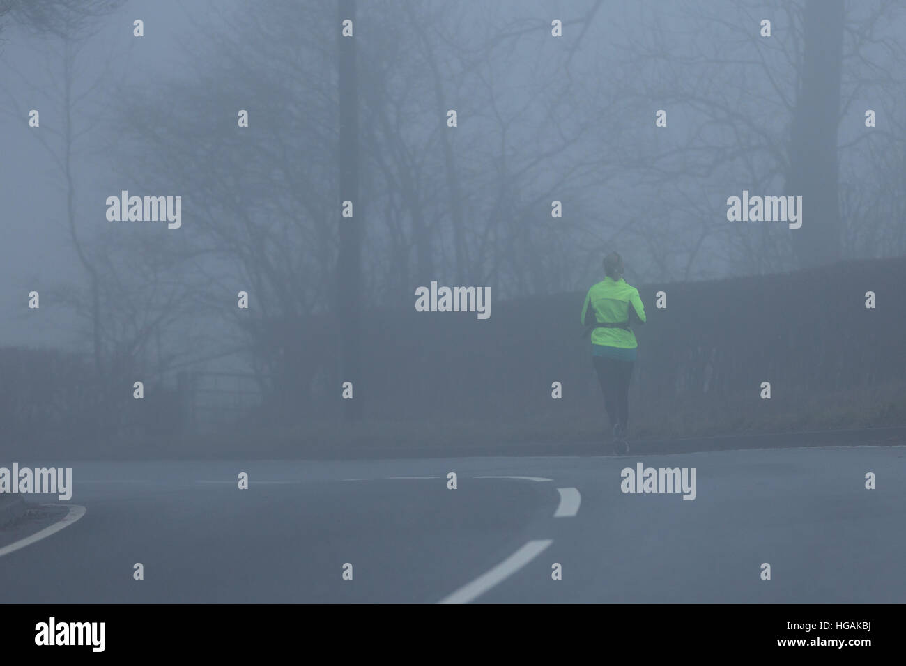 A female jogger wearing Hi Viz while jogging along the B4343 as the thick fog hampers visibility this morning. © Ian Jones/Alamy Live News Stock Photo