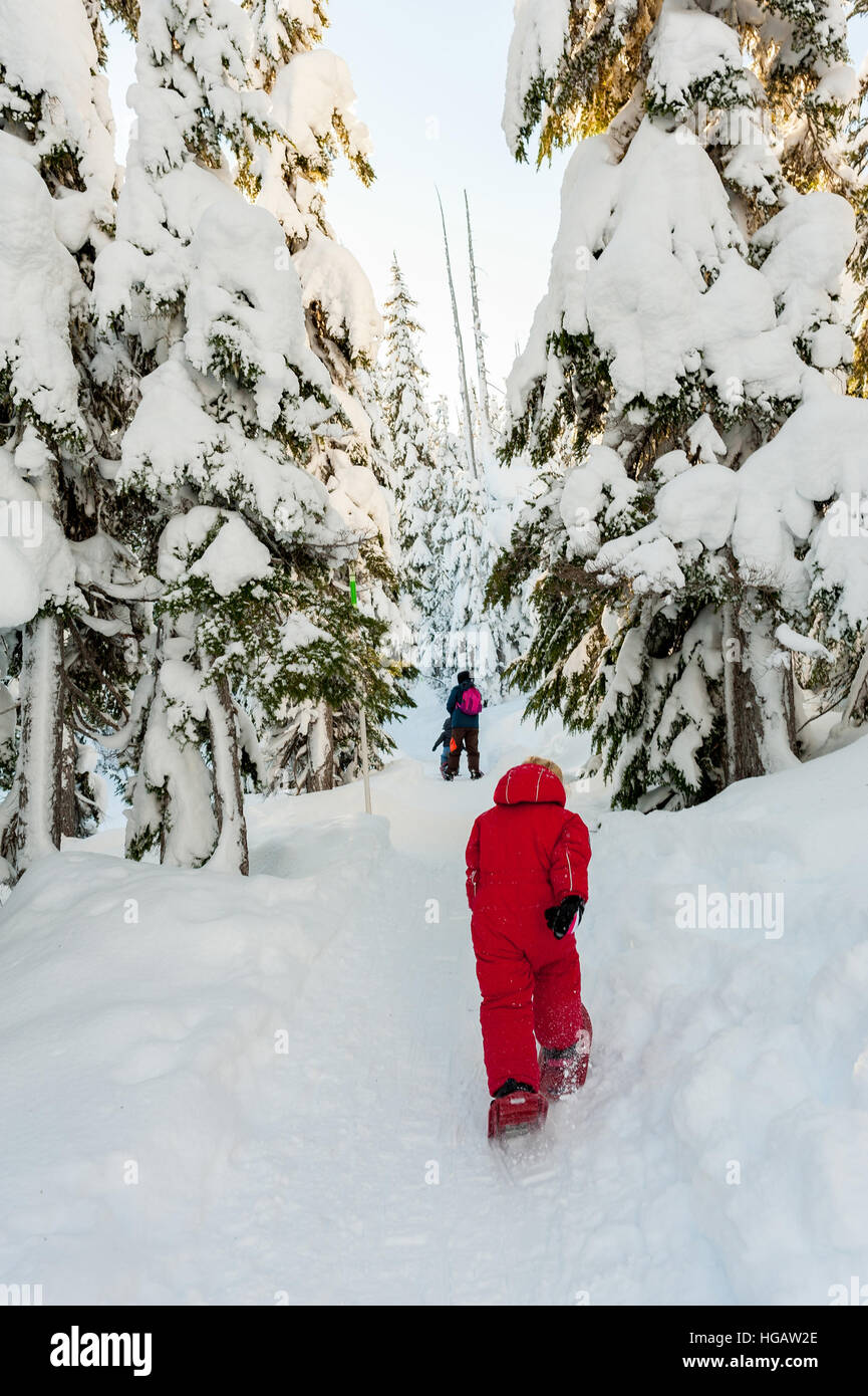A young caucasian girl in a red snowsuit snowshoeing on a snowshoe