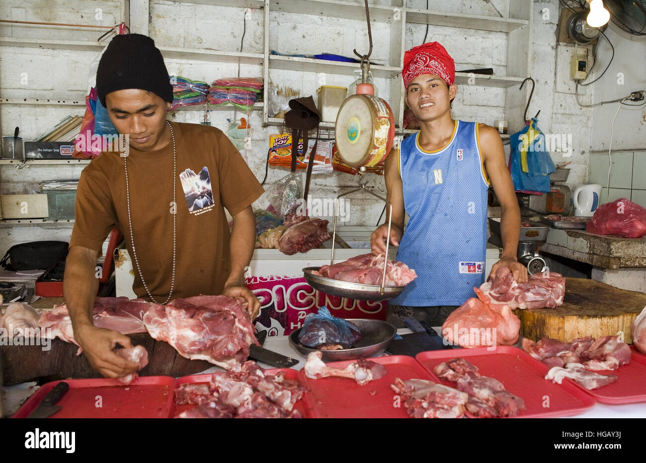 Two Filipino teenage boys sell raw meat from their stall at the meat market in Barretto, Luzon, Philippines. Stock Photo