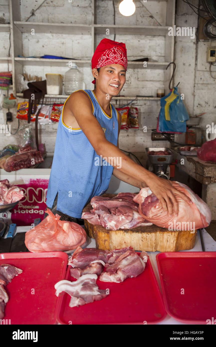 A teenage Filipino boy prepares raw pork for sale at the public market in Barretto, Luzon Island, Philippines. Stock Photo