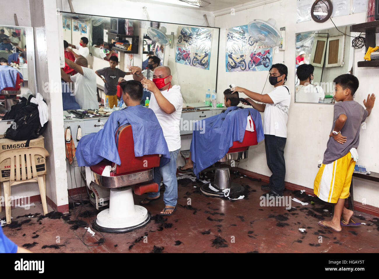 Barbers cutting customer hair inside a barbershop in Barretto Town, Subic Bay, Luzon Island, Philippines. Stock Photo