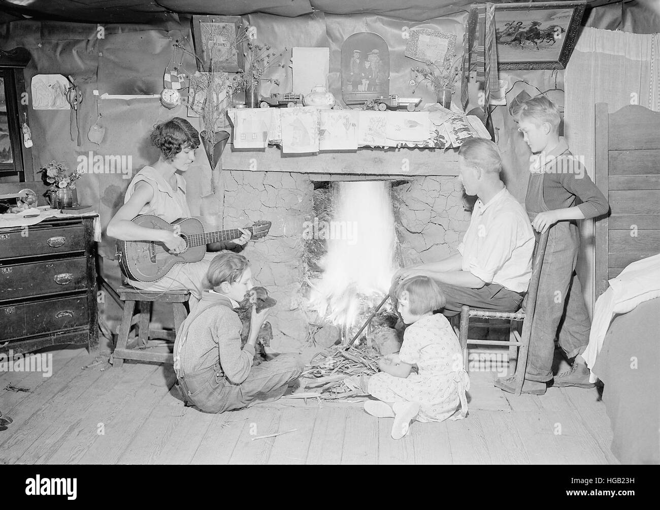 Mother plays the guitar while family gathers around the fireplace, 1933. Stock Photo