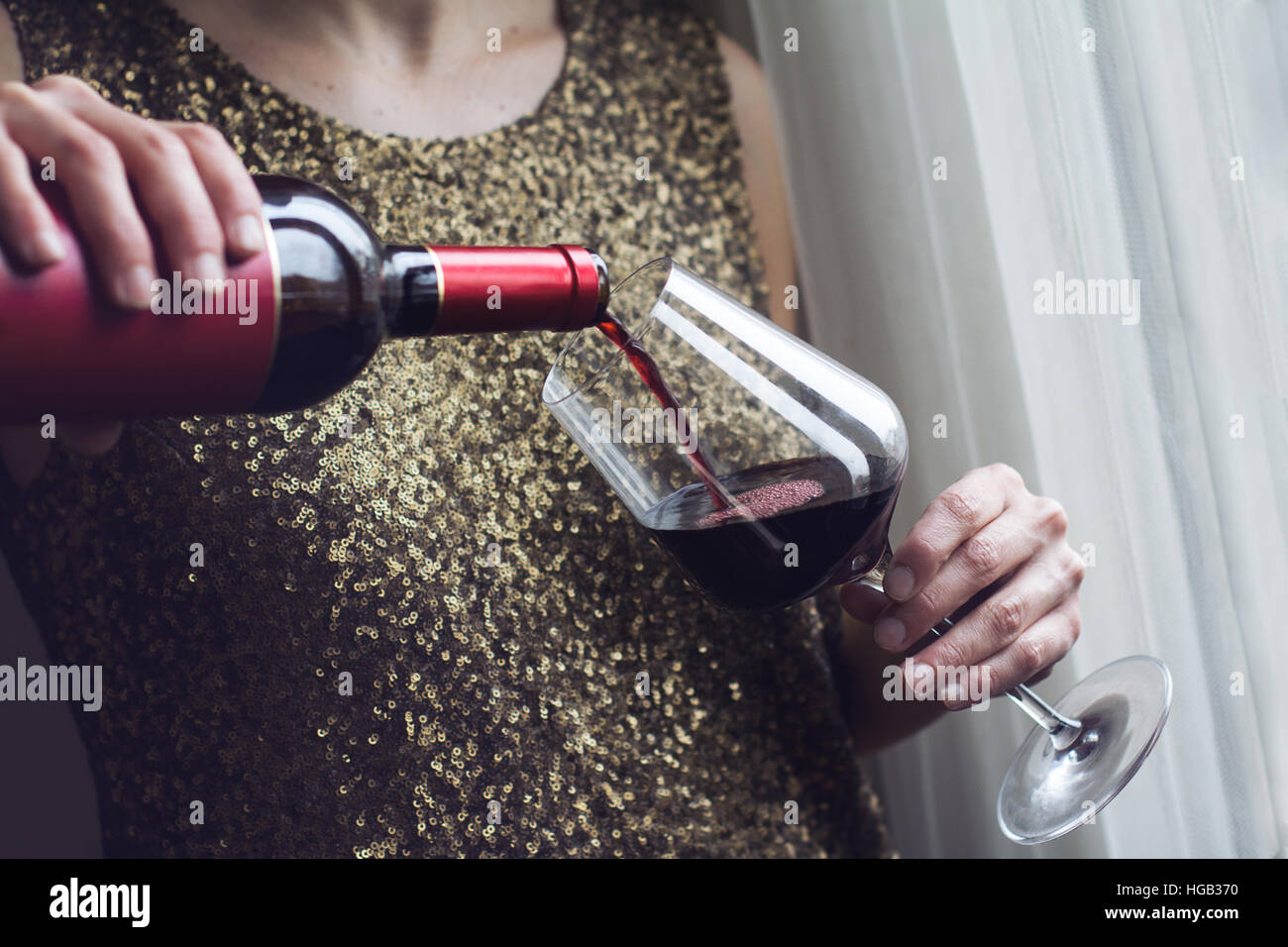 Horizontal close up of Caucasian retro woman in gold sequin vintage dress pouring red wine into a tall glass in a bar Stock Photo