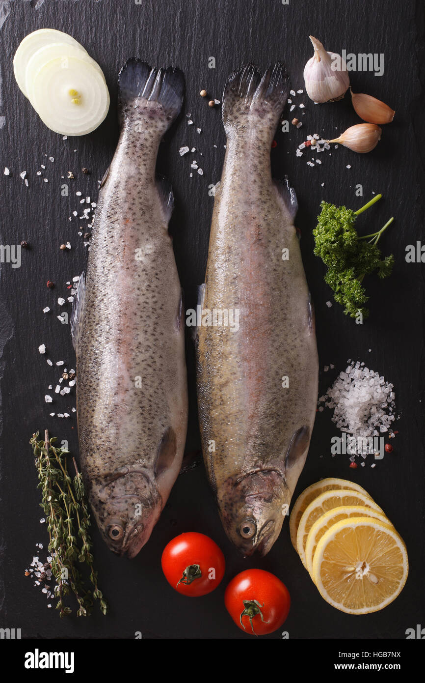 Two raw rainbow trout with ingredients on a slate board closeup. vertical top view Stock Photo