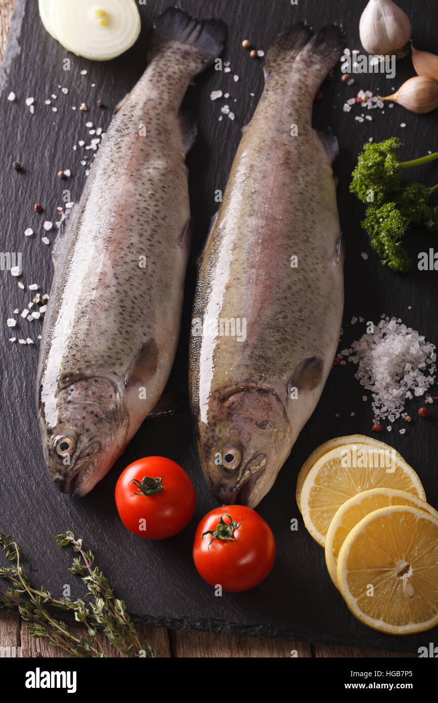 Two raw rainbow trout with ingredients on a slate board closeup. vertical Stock Photo
