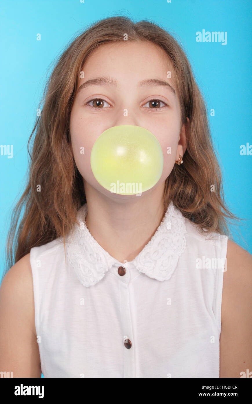 Young girl making a big bubble with a chewing gum isolated on blue