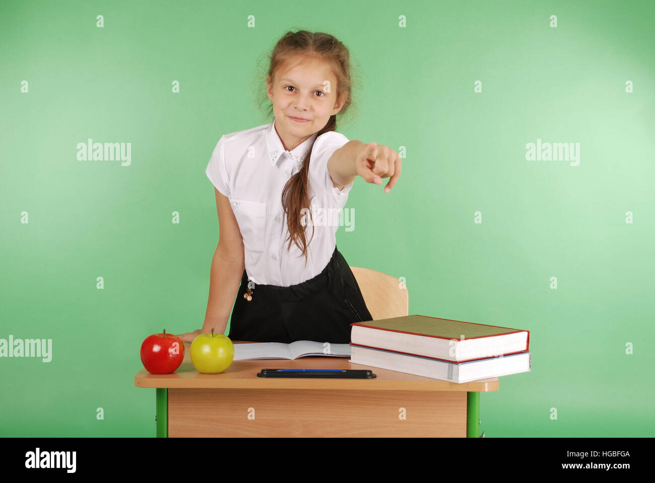 Girl in a school uniform sitting at a desk and points isolated on green