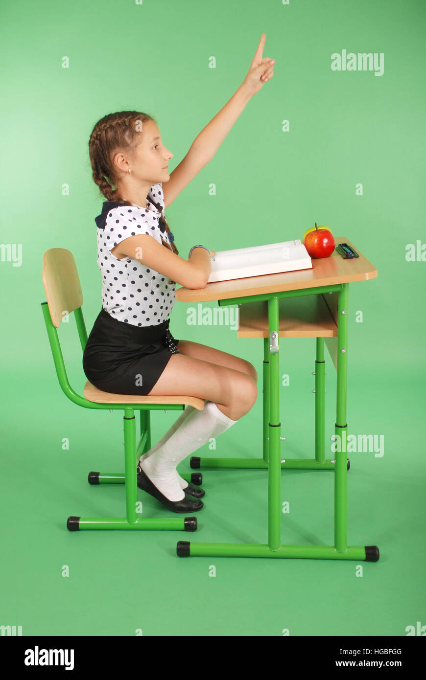 Girl in a school uniform raising hand to ask question isolated on green